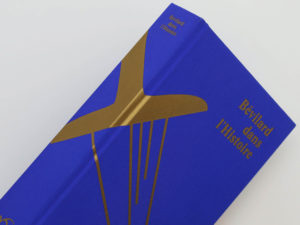 Tranche de couverture du livre Bévilard dans l'Histoire sur laquelle figure une sérigraphie dorée. Le livre est recouvert d'une toile bleu roi. Les couleurs bleu roi et or correspondent aux couleurs de la commune de Bévilard.